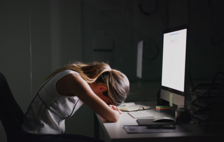 woman with head down on arms in front of computer representing work burnout