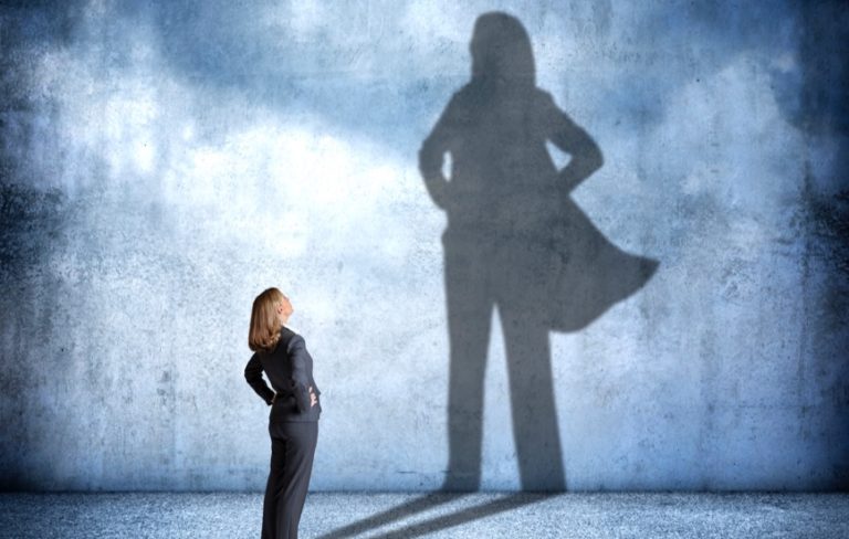 business woman with superhero shadow on the wall behind her representing hero of hybrid work
