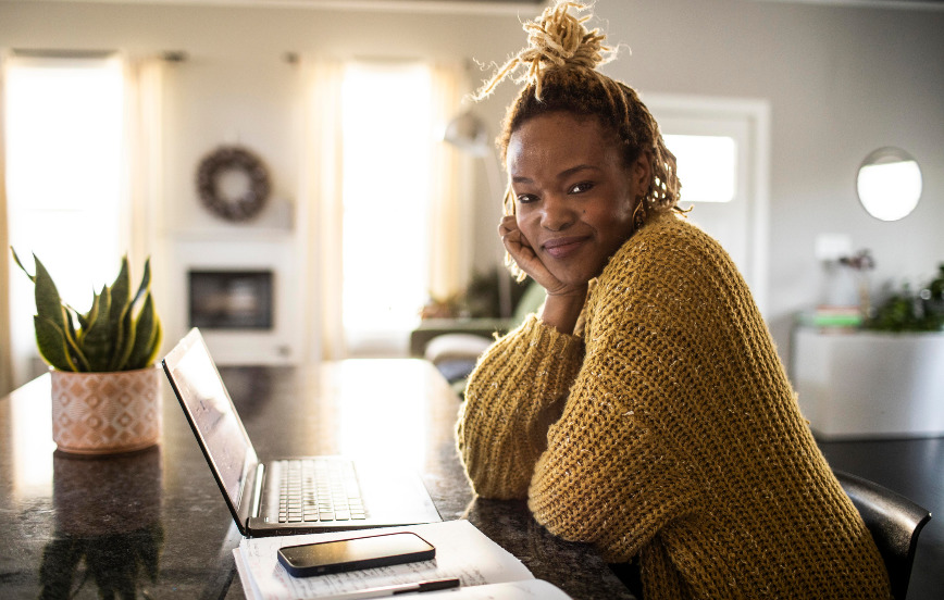 woman of color with subtle smile turned towards lens in front of laptop computer representing work from anywhere