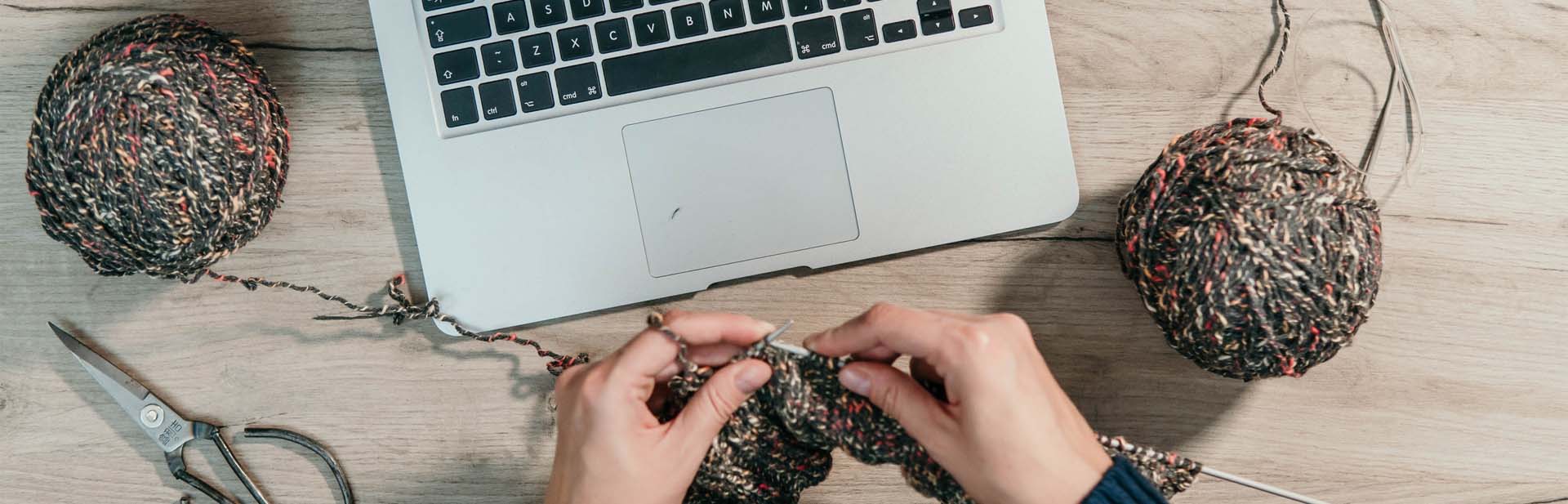 person knitting yarn in front of laptop computer