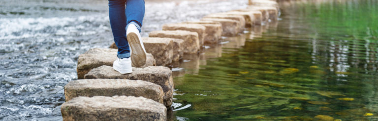 woman's feet on stepping stones crossing a river