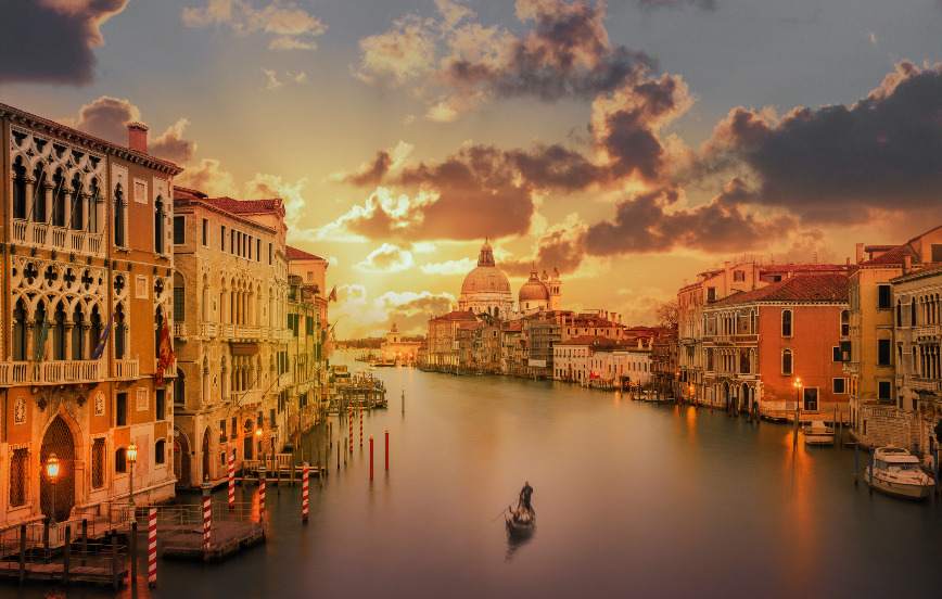 sunset view of gondolier rowing down Venice grand canal to basilica