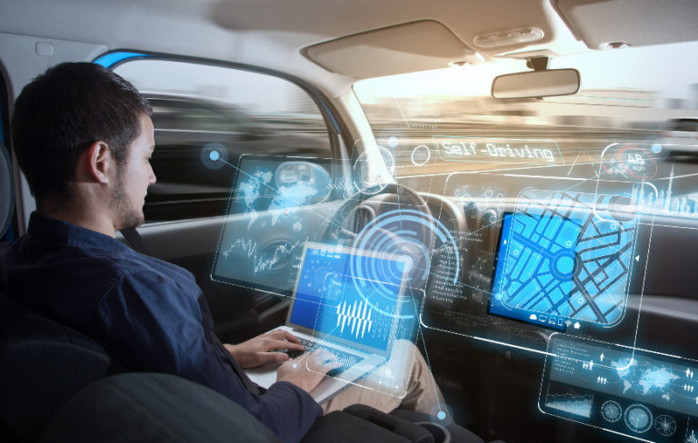 young man riding in autonomous car working on laptop with futuristic displays